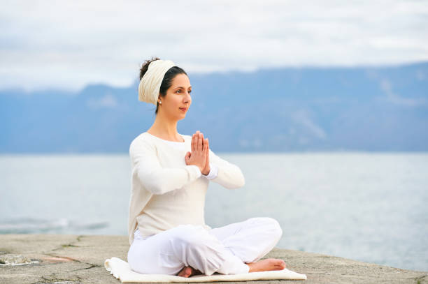 Concentrated woman meditating by the sea or lake, wearing white clothes