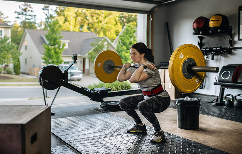 Fit woman performing front squat with heavy barbell in her home garage gym during covid-19 pandemic.